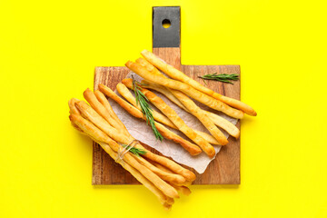 Wooden board with tasty Italian Grissini on yellow background