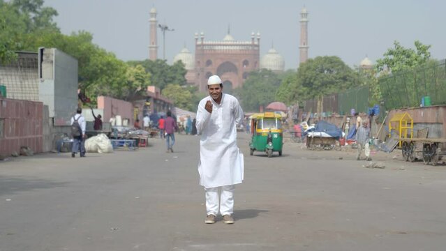 Indian muslim man doing adab to the camera in front of a mosque