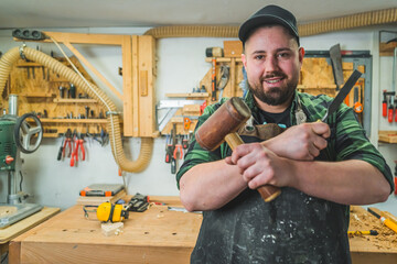 Man working as carpenter posing with chisel and mallet in front of his work table. Blue collar jobs and hobbies. High quality photo