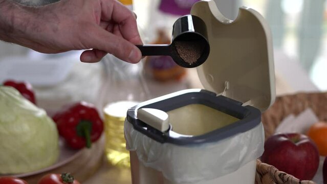 Male person pouring bokashi bran in a compost bin at home. The cook recycling compostable food leftovers into natural fertilizer