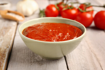 Bowl with tasty tomato paste on light wooden background, closeup