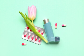 Asthma inhaler with pills and tulip on green background