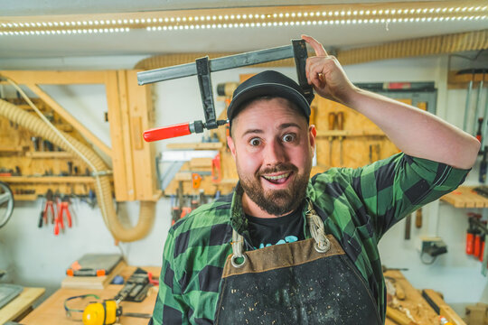 Funny positive male carpenter holding bar clamp on his head. Wood expert pretending to glue his head with professional bar clamps. High quality photo