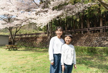 桜の下で記念撮影をする小学生の男女
