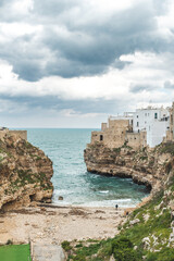 Polignano a Mare, Bari, Italy. Old town built on the rocky cliffs. Traveling concept background with old traditional houses, dramatic cloudy sky and beautiful view of Mediterranean Sea, vertical