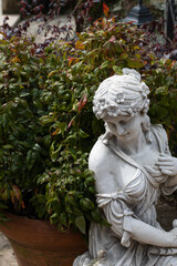 white rusty female statue placed next to potted plants