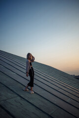 Beautiful woman on the rooftop posing at sunset. A young woman enjoys the atmosphere of the city of freedom. Relaxation concept, people, lifestyle.
