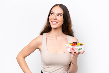 Young caucasian woman holding a bowl of fruit isolated on white background thinking an idea while looking up