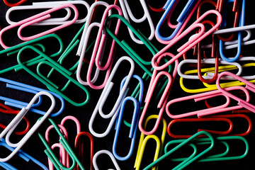 Color paper clips background. Office utensils texture. Business pattern. Isolated on black. Dark office background. Rainbow colors business design.