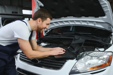 Auto service, repair, maintenance concept. mechanic checks the car, making diagnostics with laptop at the service station. Service maintenance of industrial to engine repair.