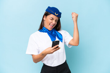 Airplane stewardess caucasian woman isolated on blue background with phone in victory position