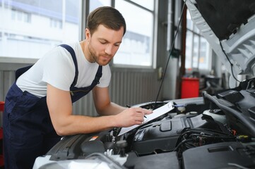 Fototapeta na wymiar car mechanic writing while holding clipboard near cars