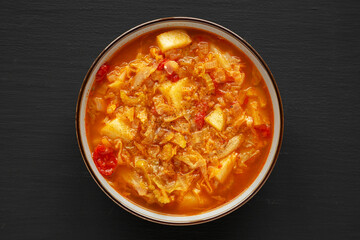 Homemade Shredded Cabbage and Potato Soup in a Bowl on a black background, top view. Overhead, from above, flat lay.