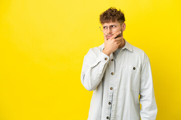 Young handsome caucasian man isolated on yellow background having doubts and with confuse face expression
