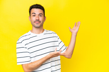 Young handsome man over isolated yellow background extending hands to the side for inviting to come