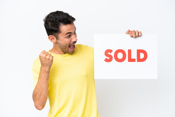 Young handsome man over isolated white background holding a placard with text SOLD and celebrating a victory