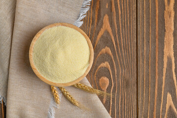 Bowl of raw semolina and spikelets on wooden background