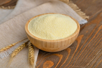 Bowl of raw semolina and spikelets on wooden background