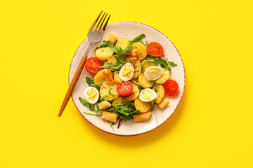 Plate of tasty potato salad with eggs and tomatoes on yellow background, top view