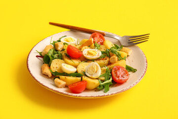 Plate of tasty potato salad with eggs and tomatoes on yellow background