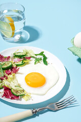 Plate with tasty fried egg and salad on blue background