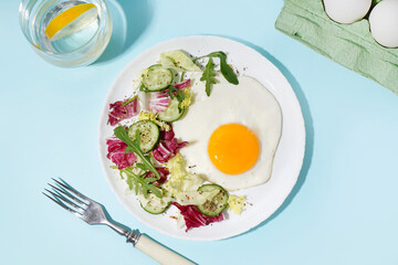 Plate with tasty fried egg and salad on blue background