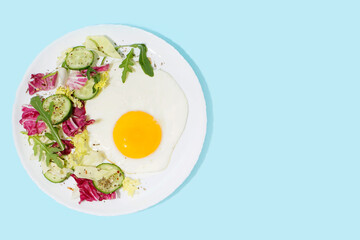 Plate with tasty fried egg and salad on blue background