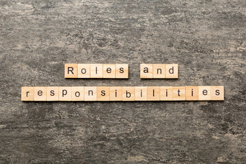 roles and responsibilities word written on wood block. roles and responsibilities text on table,...