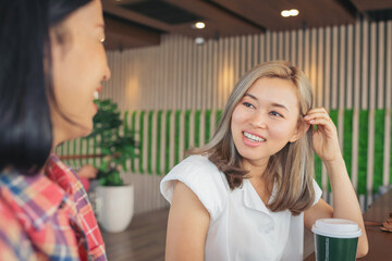 Two girl friends drinking coffee in the cafe. Two women at cafe, talking, laughing and enjoying their time. Lifestyle and friendship concepts with real people models.