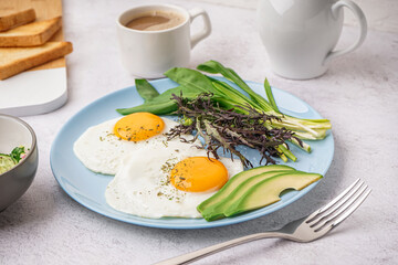 Plate with tasty fried eggs, coffee and greens on light table