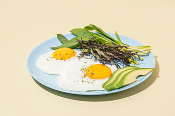 Plate with tasty fried eggs and greens on beige background