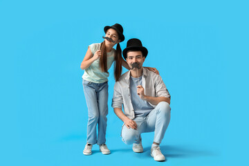 Portrait of father and his little daughter with paper mustache on light blue background