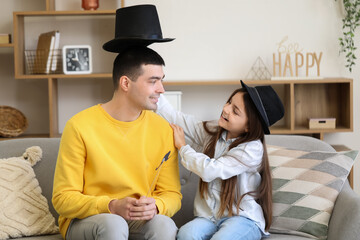 Portrait of father and his little daughter with paper mustache sitting on sofa at home
