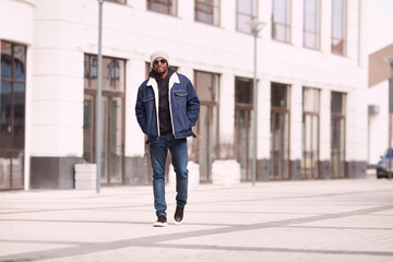 Serious modern fashion man in stylish denim clothes walks in urban street, full length