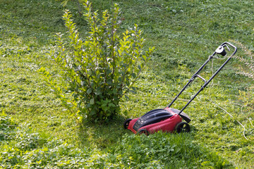 The lawnmower is standing on the grass in the garden. Grass mowing, yard and garden care.