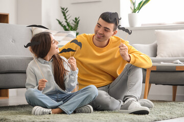 Portrait of father and his little daughter with paper mustache at home