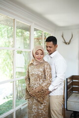 A man and a woman stand in front of a window, one of them is wearing a gold dress.