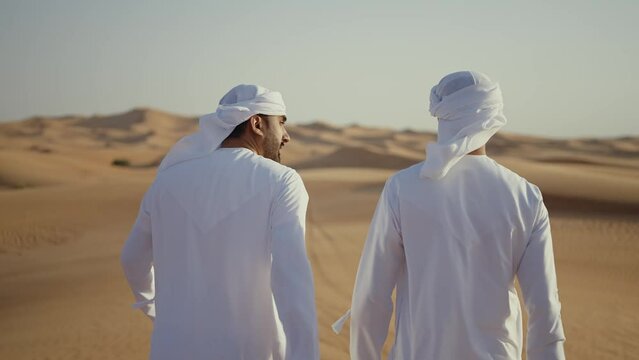 Two friends making the safari in the Dubai desert. Locals with kandura white outfit spending time together on the dunes in sharjah. Concept about traveling in the united arab emirates
