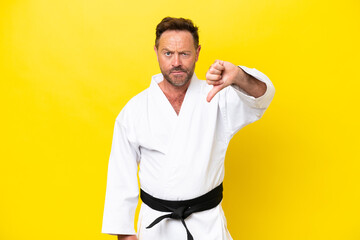 Middle age caucasian man doing karate isolated on yellow background showing thumb down with negative expression