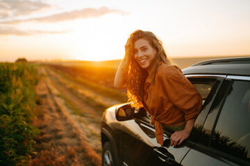 Young happy woman leaning out of the car window enjoying the sunset. The concept of active...