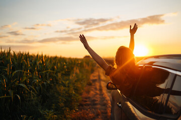 Young happy woman leaning out of the car window enjoying the sunset. The concept of active...