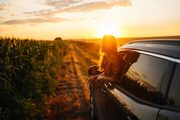 Young happy woman leaning out of the car window enjoying the sunset. The concept of active...