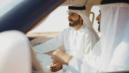 Two friends making the safari in the Dubai desert. Locals with kandura white outfit spending time together with the 4x4 car on the dunes in sharjah. Concept about traveling in the united arab emirates