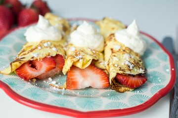 Plate with strawberry crepes with whipped cream topping