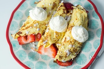 Plate with strawberry crepes with whipped cream topping