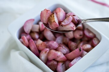 Closeup of the spoon with red sliced potatoes with the background of a bowl of red sliced potatoes