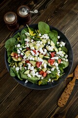 Vertical top view of good-looking salad with a wooden spoon and fork near the spice containers