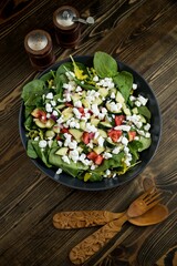 Vertical top view of a good-looking salad with a wooden spoon and fork near the spice containers