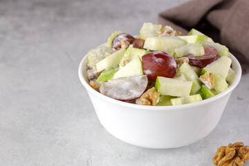 Bowl of waldorf salad with apple, celery, grapes, walnuts and yogurt on a white background. Copy space.