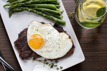 Closeup of the steak with egg and asparagus on a white plate with Mojito on a wooden table